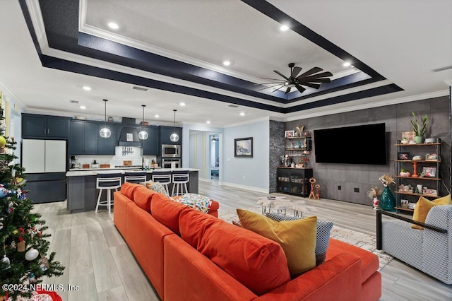 living room with ceiling fan, light wood-type flooring, crown molding, and a tray ceiling