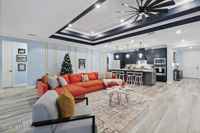 living room featuring a raised ceiling, light wood-type flooring, and ornamental molding