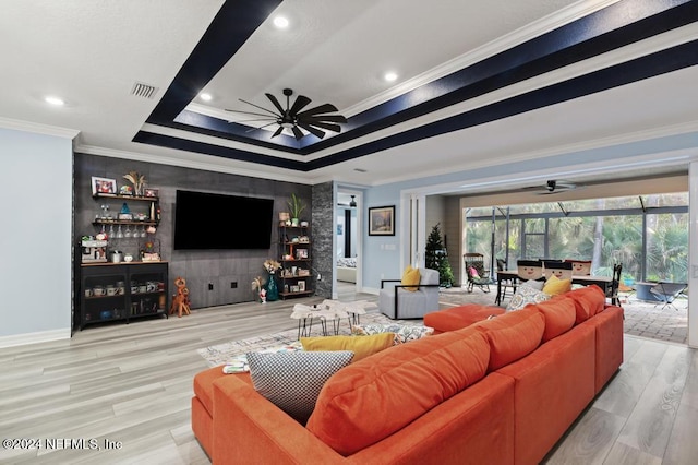 living room with light hardwood / wood-style flooring, a raised ceiling, ceiling fan, and ornamental molding