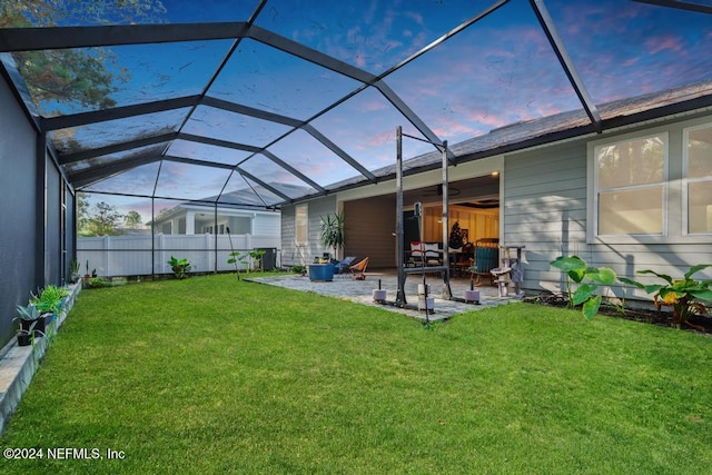 back house at dusk featuring a patio, a lanai, and a lawn