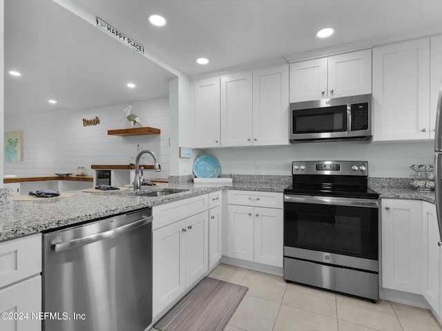 kitchen featuring appliances with stainless steel finishes, white cabinets, light stone countertops, and sink