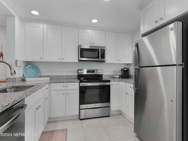 kitchen featuring appliances with stainless steel finishes, light stone countertops, light tile patterned floors, sink, and white cabinetry