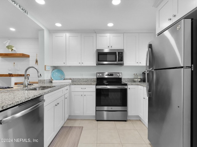 kitchen with stainless steel appliances, light stone counters, white cabinets, light tile patterned flooring, and sink