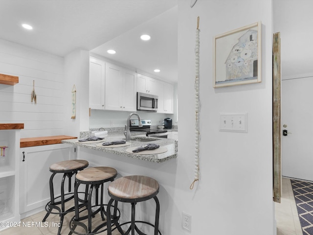 kitchen featuring stainless steel appliances, a kitchen bar, white cabinetry, and light stone countertops