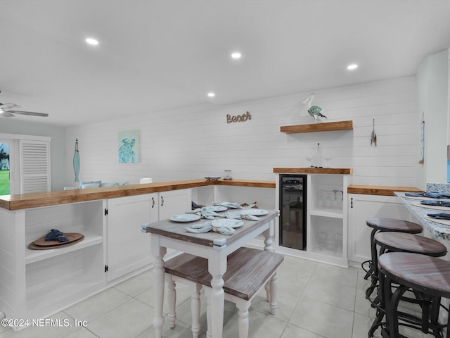 kitchen featuring beverage cooler, ceiling fan, white cabinets, light tile patterned flooring, and butcher block counters