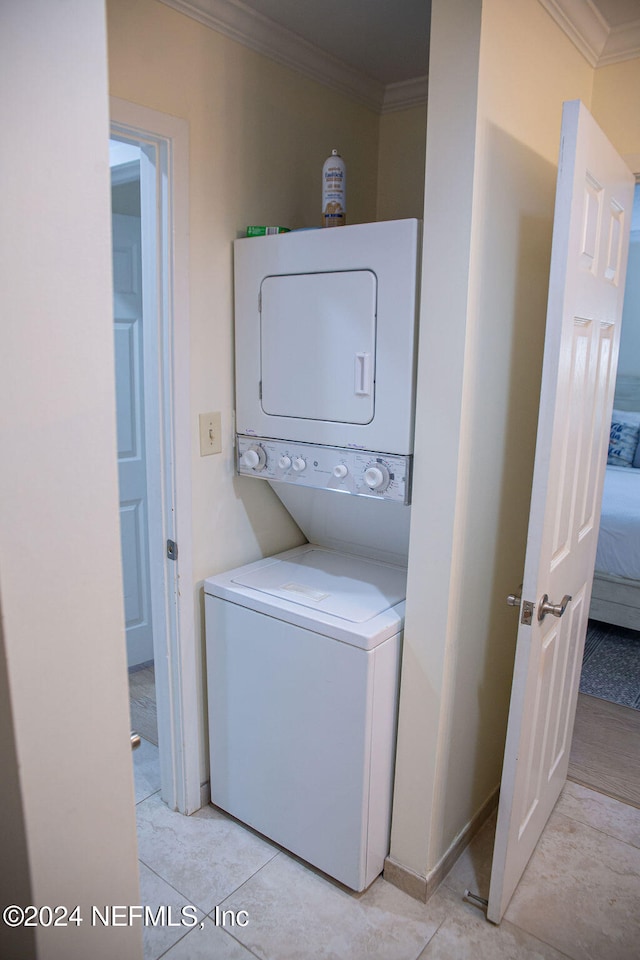 clothes washing area featuring ornamental molding, light tile patterned floors, and stacked washer and clothes dryer