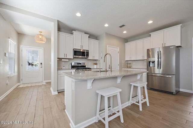 kitchen with stainless steel appliances, white cabinetry, a center island with sink, and sink