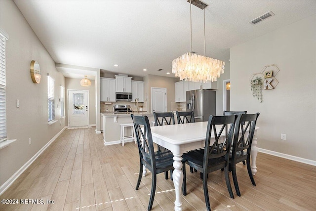 dining space with a chandelier, a textured ceiling, and light wood-type flooring