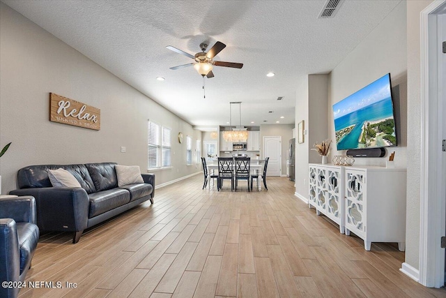 living room with ceiling fan, a textured ceiling, and light wood-type flooring