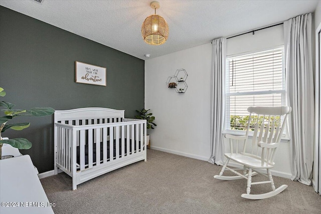 carpeted bedroom featuring a textured ceiling and a nursery area