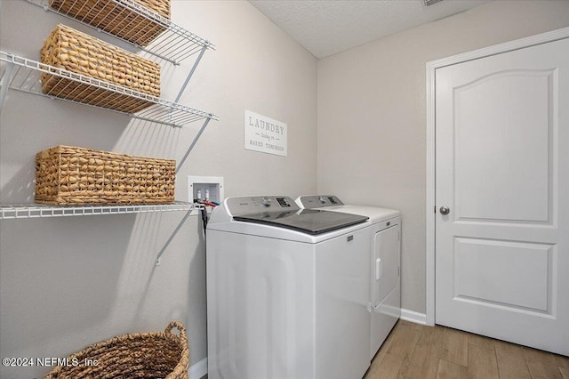 clothes washing area featuring washer and dryer, a textured ceiling, and light hardwood / wood-style flooring