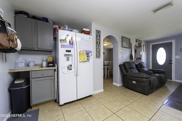 kitchen featuring gray cabinets, white refrigerator with ice dispenser, a textured ceiling, and light tile patterned floors