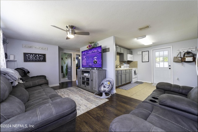 living room featuring ceiling fan, light hardwood / wood-style floors, and a textured ceiling