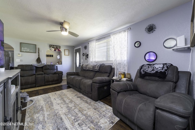 living room featuring a textured ceiling, ceiling fan, and dark wood-type flooring