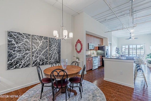 dining space with a towering ceiling, ceiling fan with notable chandelier, and dark wood-type flooring