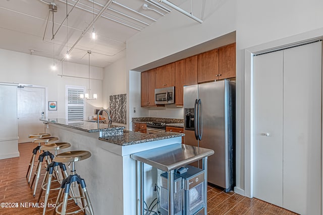 kitchen with appliances with stainless steel finishes, a kitchen breakfast bar, a center island with sink, dark stone countertops, and dark hardwood / wood-style floors