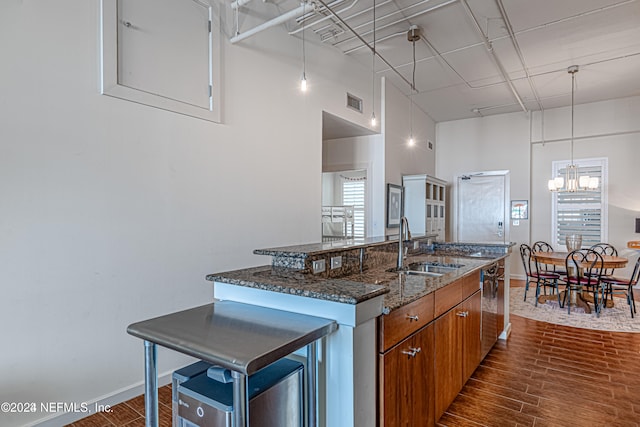 kitchen with a towering ceiling, dark wood-type flooring, sink, a center island with sink, and a chandelier