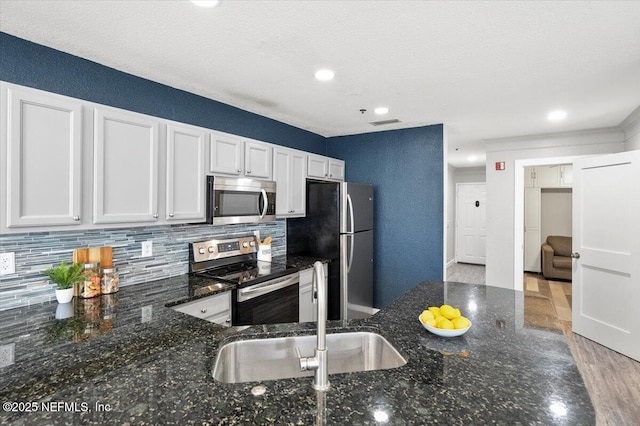 kitchen with stainless steel appliances, white cabinetry, and dark stone counters