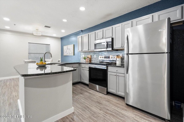 kitchen with appliances with stainless steel finishes, sink, decorative backsplash, kitchen peninsula, and light wood-type flooring