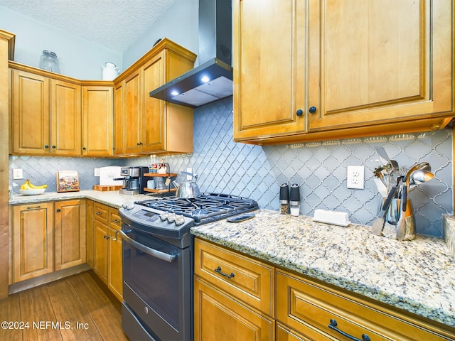 kitchen with backsplash, wall chimney range hood, hardwood / wood-style flooring, a textured ceiling, and range with gas stovetop