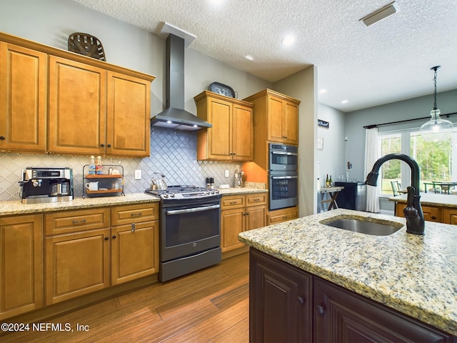 kitchen with dark hardwood / wood-style flooring, wall chimney exhaust hood, stainless steel appliances, sink, and decorative light fixtures