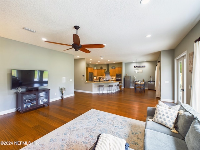 living room featuring a textured ceiling, ceiling fan, and dark wood-type flooring