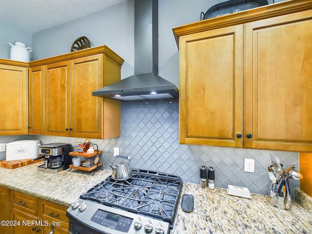 kitchen featuring tasteful backsplash, wall chimney exhaust hood, a textured ceiling, and stainless steel range with gas stovetop