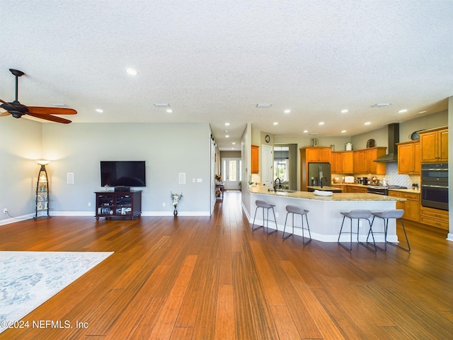 kitchen with a kitchen breakfast bar, wall chimney range hood, dark hardwood / wood-style floors, a textured ceiling, and appliances with stainless steel finishes