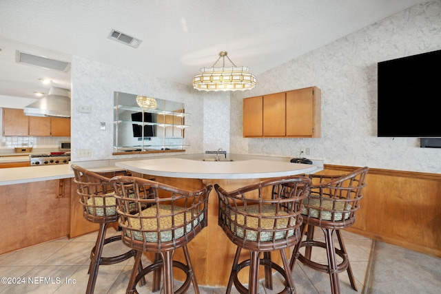 kitchen with a breakfast bar, light tile patterned floors, extractor fan, and a textured ceiling