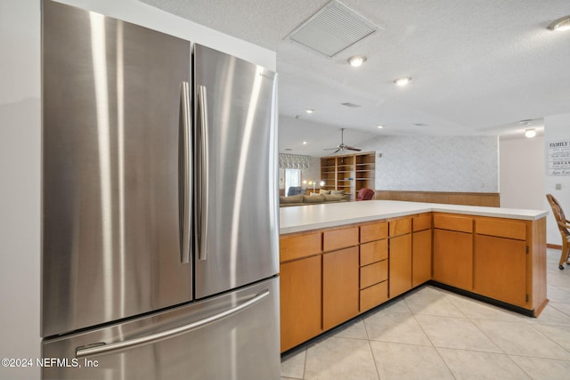 kitchen featuring kitchen peninsula, a textured ceiling, ceiling fan, light tile patterned floors, and stainless steel refrigerator