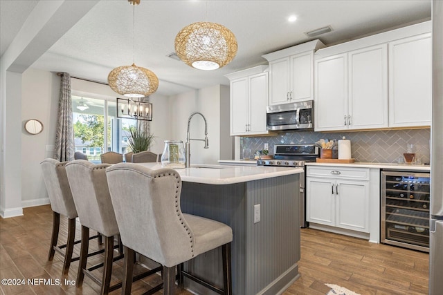 kitchen featuring pendant lighting, white cabinets, hardwood / wood-style flooring, stainless steel appliances, and beverage cooler