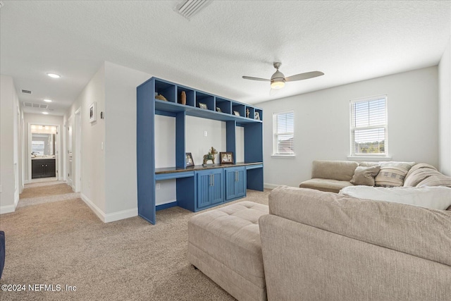 living room with a textured ceiling, light colored carpet, and ceiling fan