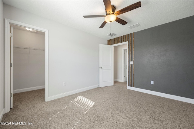 unfurnished bedroom featuring ceiling fan, a spacious closet, a textured ceiling, a closet, and carpet