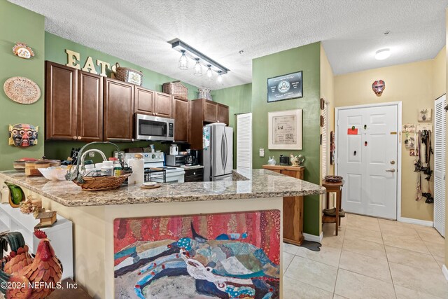 605 Fairway Dr Unit 205, Saint Augustine, FL 32084 - kitchen featuring stainless steel appliances, light tile patterned flooring, a peninsula, light stone counters, and a textured ceiling
