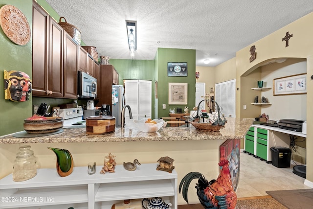 kitchen with light stone countertops, stainless steel appliances, kitchen peninsula, a textured ceiling, and light tile patterned floors