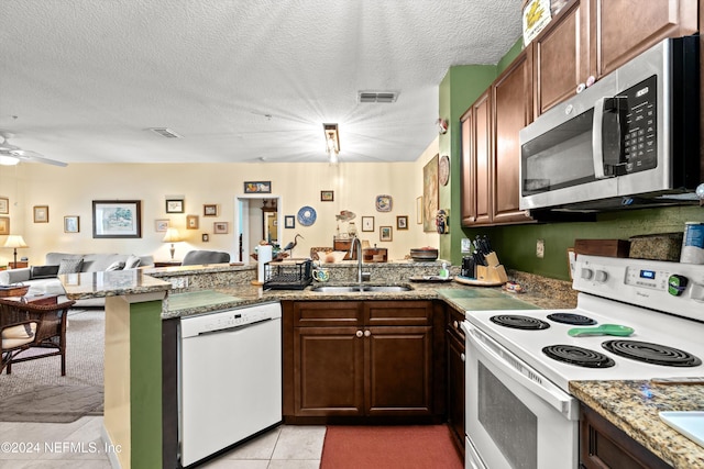 kitchen with white appliances, sink, light tile patterned floors, a textured ceiling, and kitchen peninsula