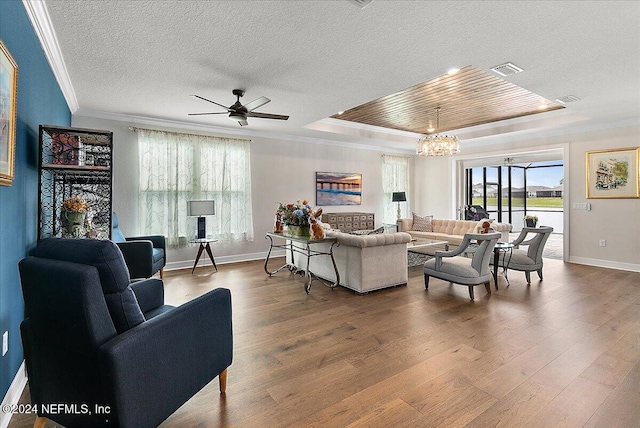 living room with ceiling fan with notable chandelier, hardwood / wood-style flooring, crown molding, and a tray ceiling