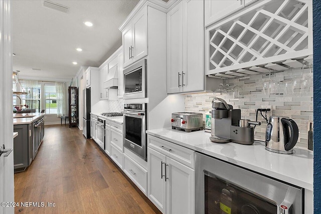 kitchen with white cabinetry, dark wood-type flooring, beverage cooler, stainless steel appliances, and backsplash