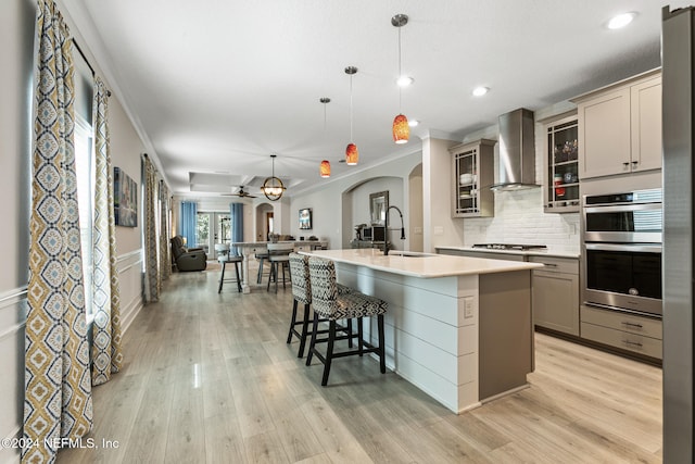 kitchen featuring gray cabinetry, sink, wall chimney range hood, pendant lighting, and a center island with sink