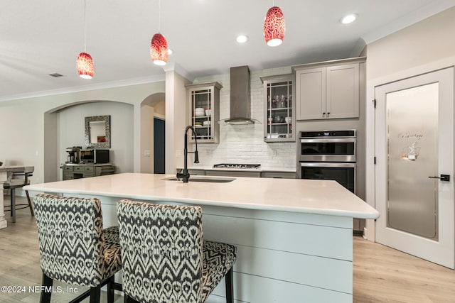 kitchen with a breakfast bar, wall chimney range hood, sink, gray cabinets, and decorative light fixtures