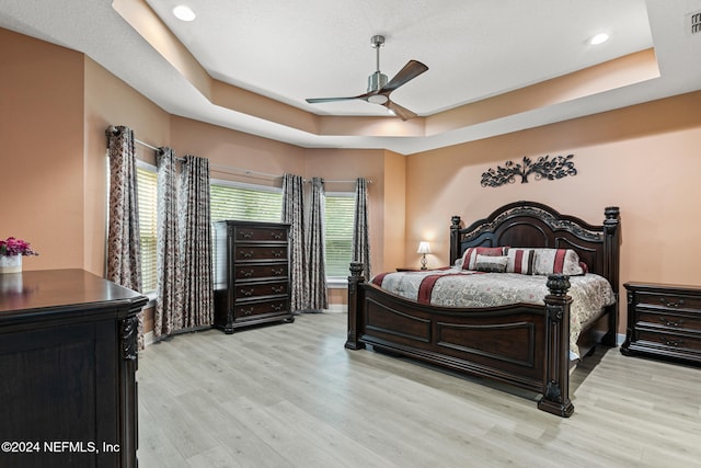 bedroom featuring ceiling fan, light hardwood / wood-style floors, a raised ceiling, and multiple windows