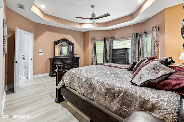 bedroom with ceiling fan, a raised ceiling, and light hardwood / wood-style flooring