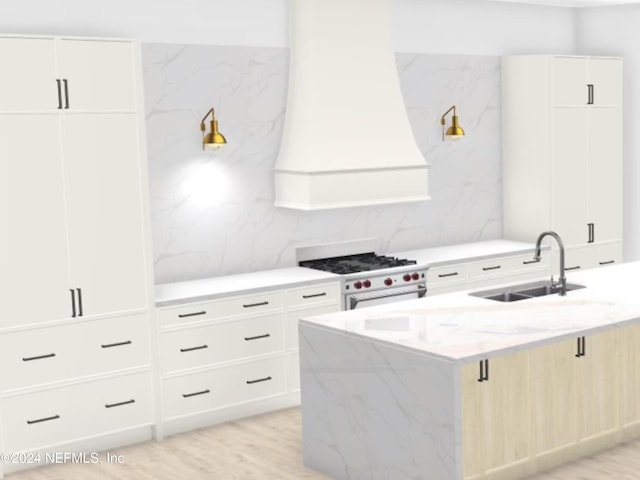 kitchen featuring white cabinetry, sink, high end white range oven, an island with sink, and light wood-type flooring