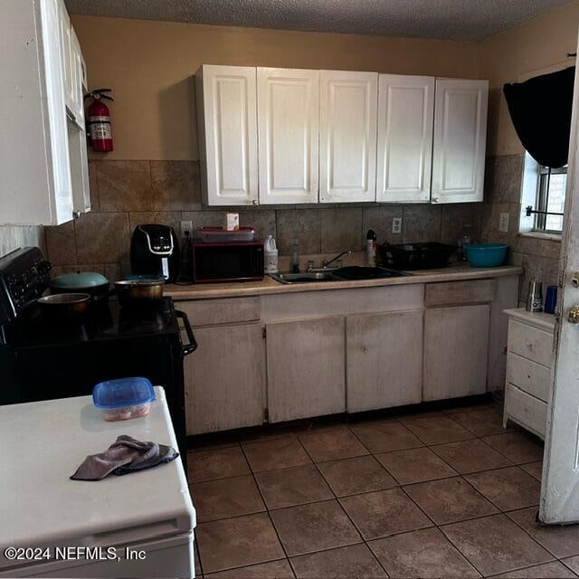 kitchen featuring white cabinetry, sink, a textured ceiling, black appliances, and dark tile patterned flooring