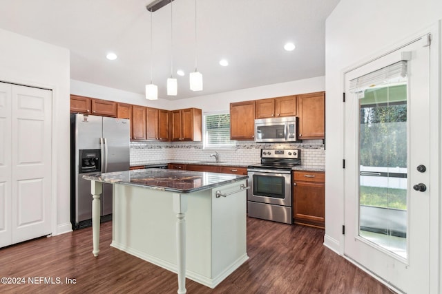 kitchen with appliances with stainless steel finishes, sink, a center island, dark hardwood / wood-style floors, and hanging light fixtures