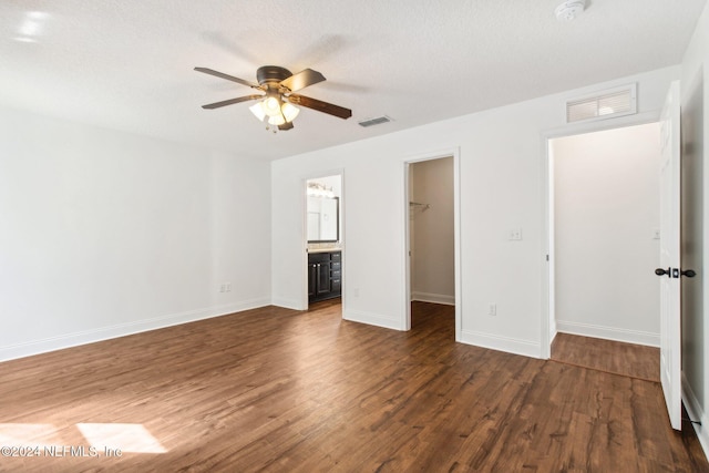 unfurnished bedroom with ceiling fan, a spacious closet, connected bathroom, dark hardwood / wood-style flooring, and a closet