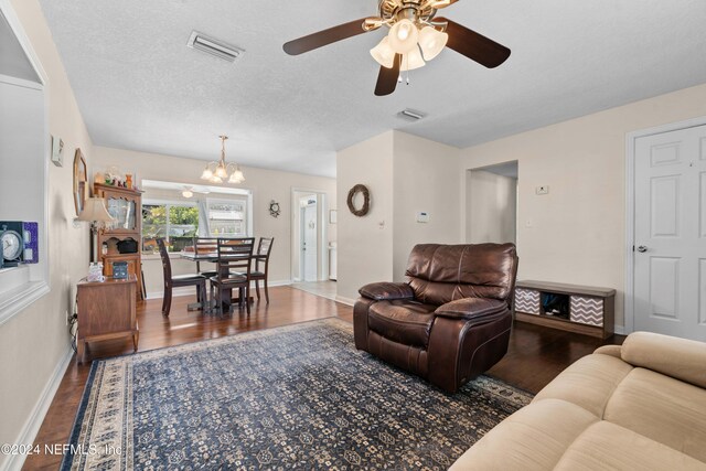 living room featuring a textured ceiling, ceiling fan with notable chandelier, and dark wood-type flooring