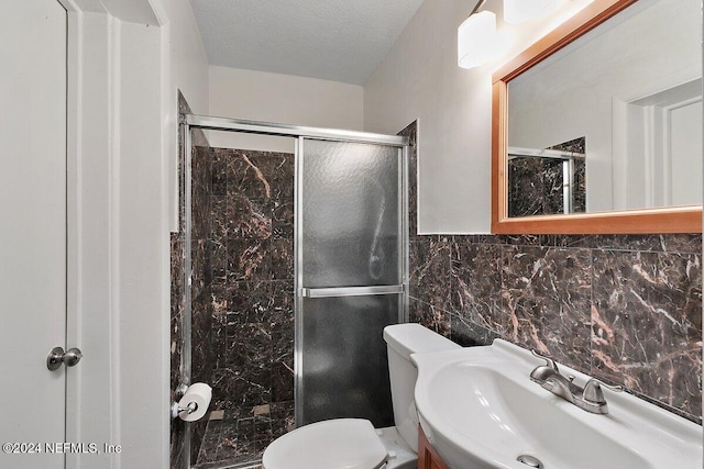 bathroom with sink, an enclosed shower, a textured ceiling, toilet, and tile walls