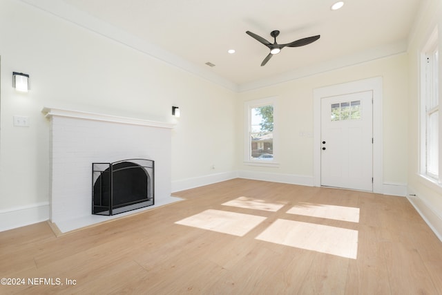 unfurnished living room with light hardwood / wood-style floors, a brick fireplace, ceiling fan, and crown molding