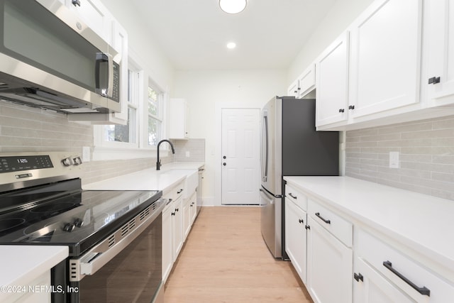 kitchen with backsplash, white cabinets, sink, appliances with stainless steel finishes, and light hardwood / wood-style floors